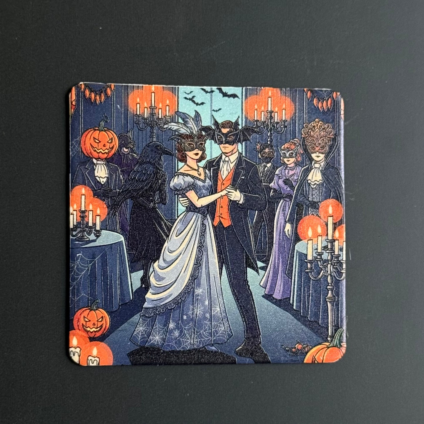 A square coaster featuring a vintage-style Halloween illustration with a dancing couple in the center, surrounded by jack-o'-lanterns, candelabras, and masked guests in a dimly lit hall.