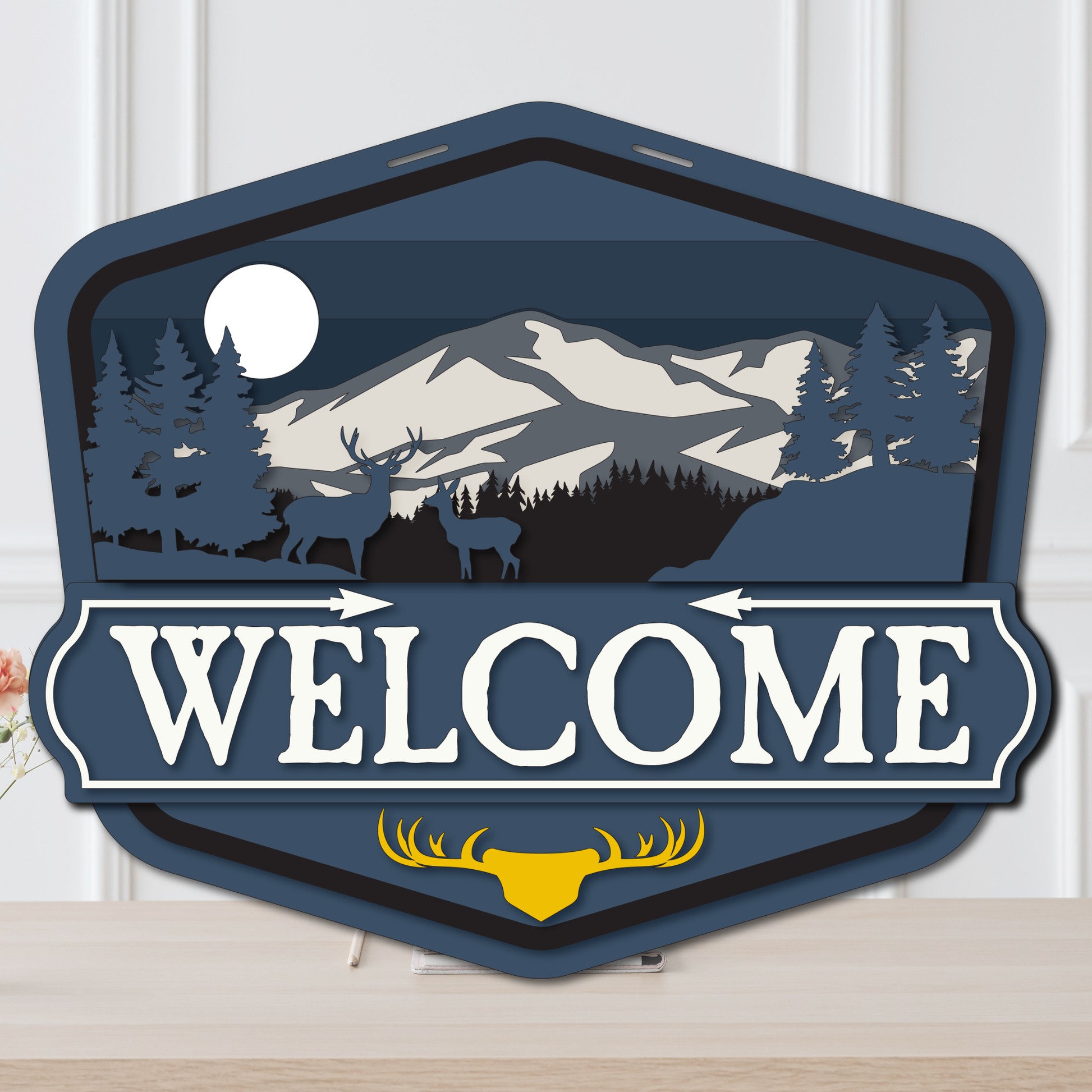 Decorative 'Welcome' sign with mountain and deer design on a white background
