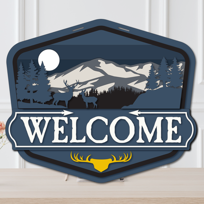 Decorative 'Welcome' sign with mountain and deer design on a white background