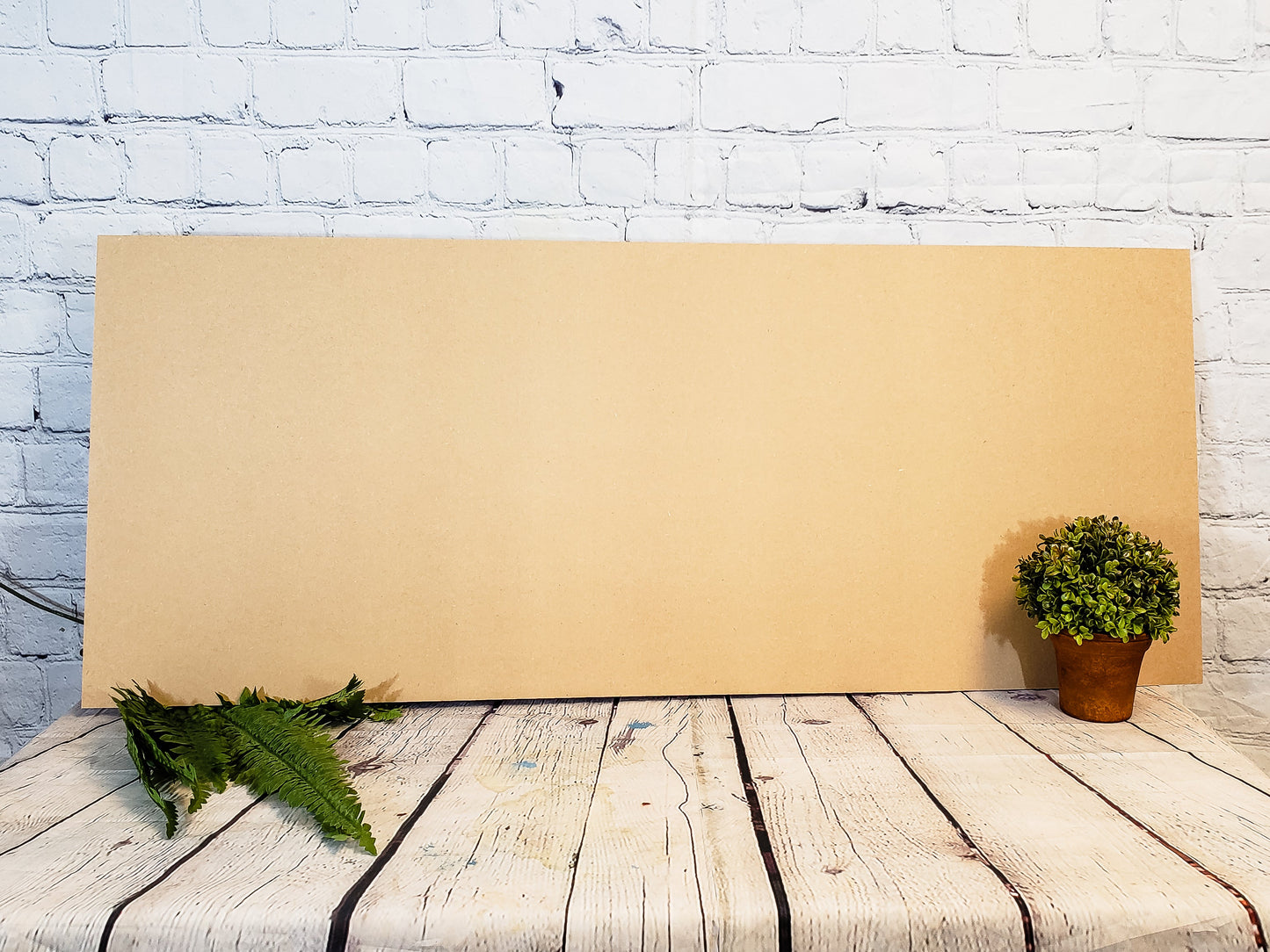 Large MDF sheet on a wooden surface with plants against a white brick wall.