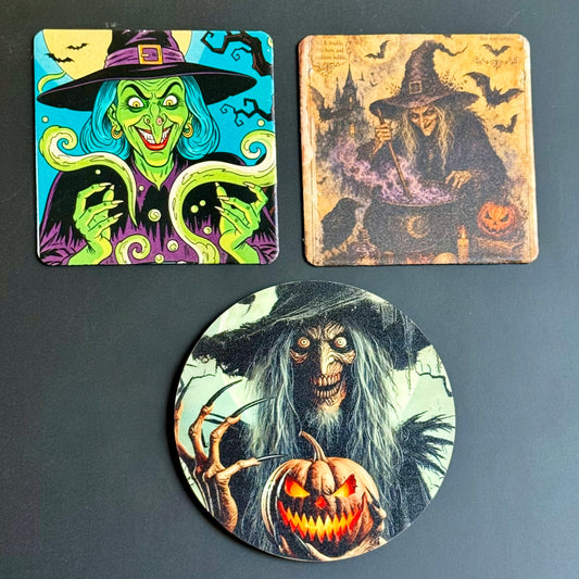 Three Halloween-themed printed coasters displayed on a dark gray surface: a square coaster with a colorful witch illustration in the top left, a square coaster with a tan-toned witch scene in the top right, and a round coaster with a creepy witch holding a jack-o'-lantern at the bottom center.