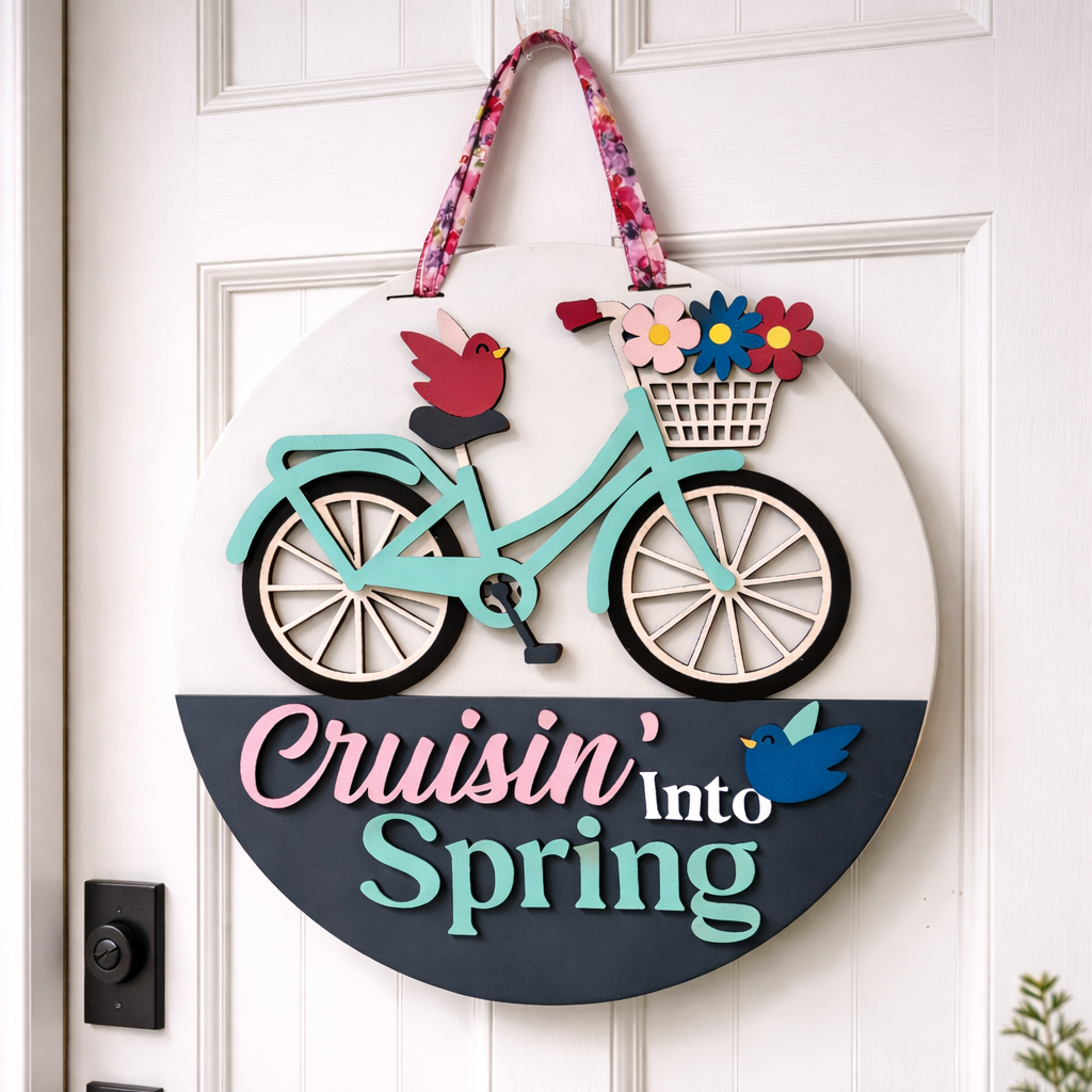 Decorative door hanger with a bicycle, flowers, and birds on a white door.