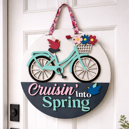 Decorative door hanger with a bicycle, flowers, and birds on a white door.