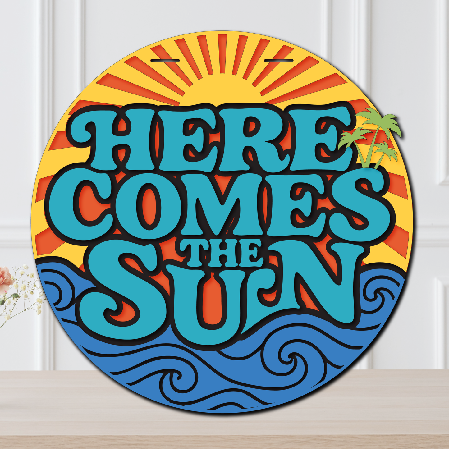 Decorative sign with 'Here Comes the Sun' text and sun design on a white background