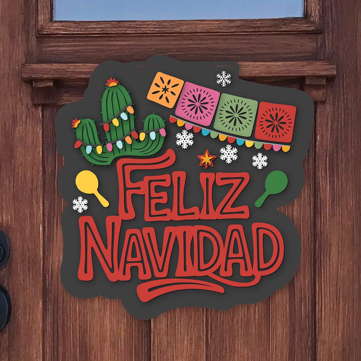 Shaped door hanger reading Feliz Navidad in bold red letters, with a cactus wrapped in colorful Christmas lights, papel picado banners, maracas and white snowflakes on a charcoal background, hanging on a wooden front door.