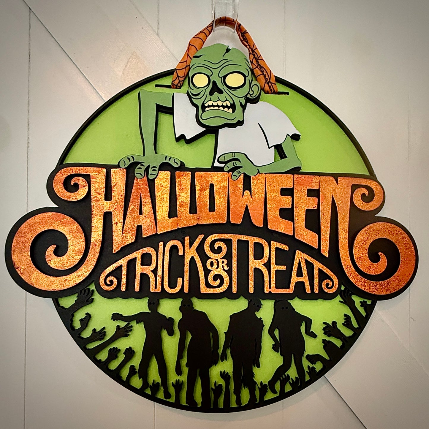Halloween-themed decorative sign with a zombie design on a white wall.