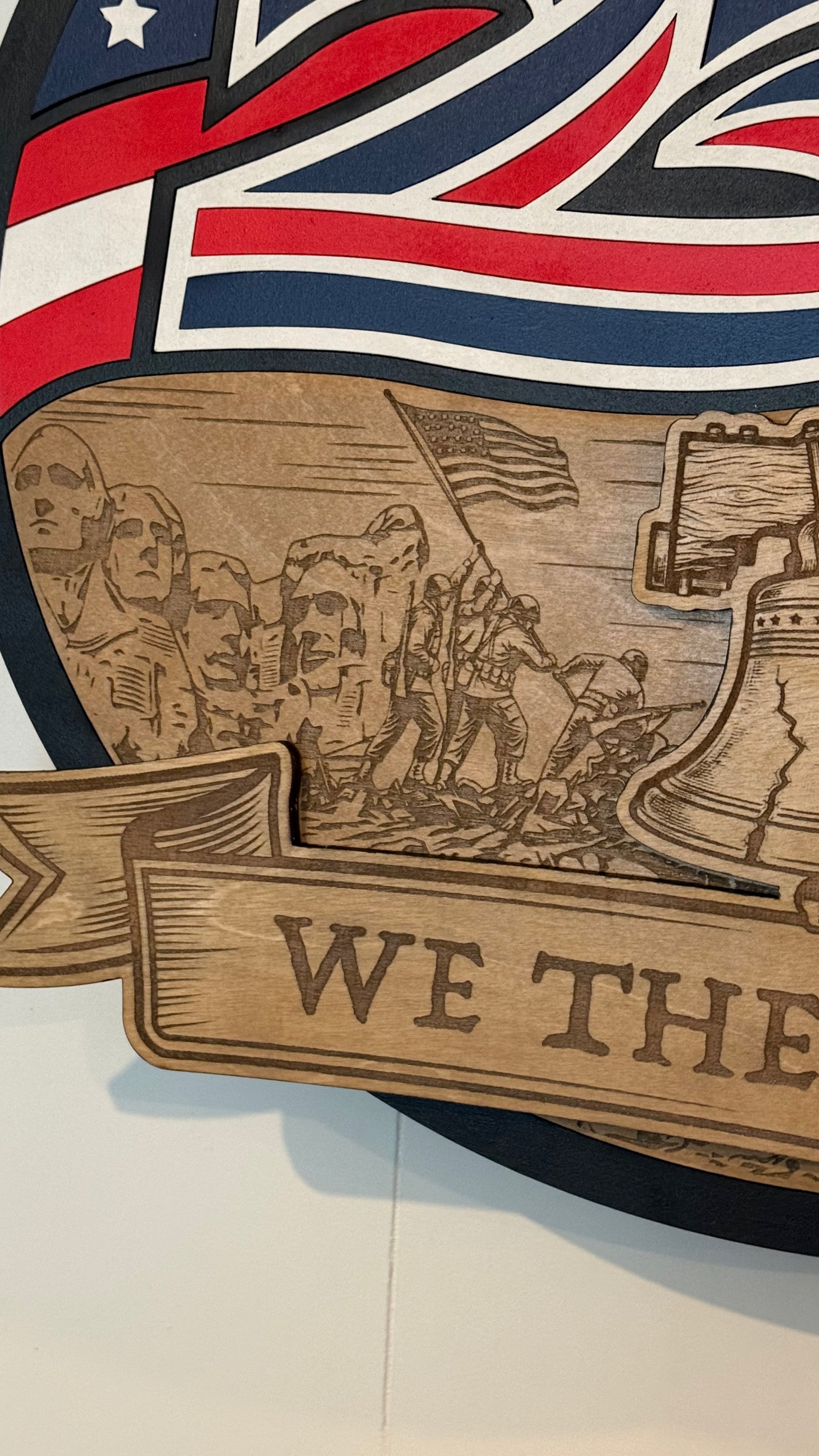 Wooden plaque with engraved image of soldiers and 'WE THE' text, American flag in background