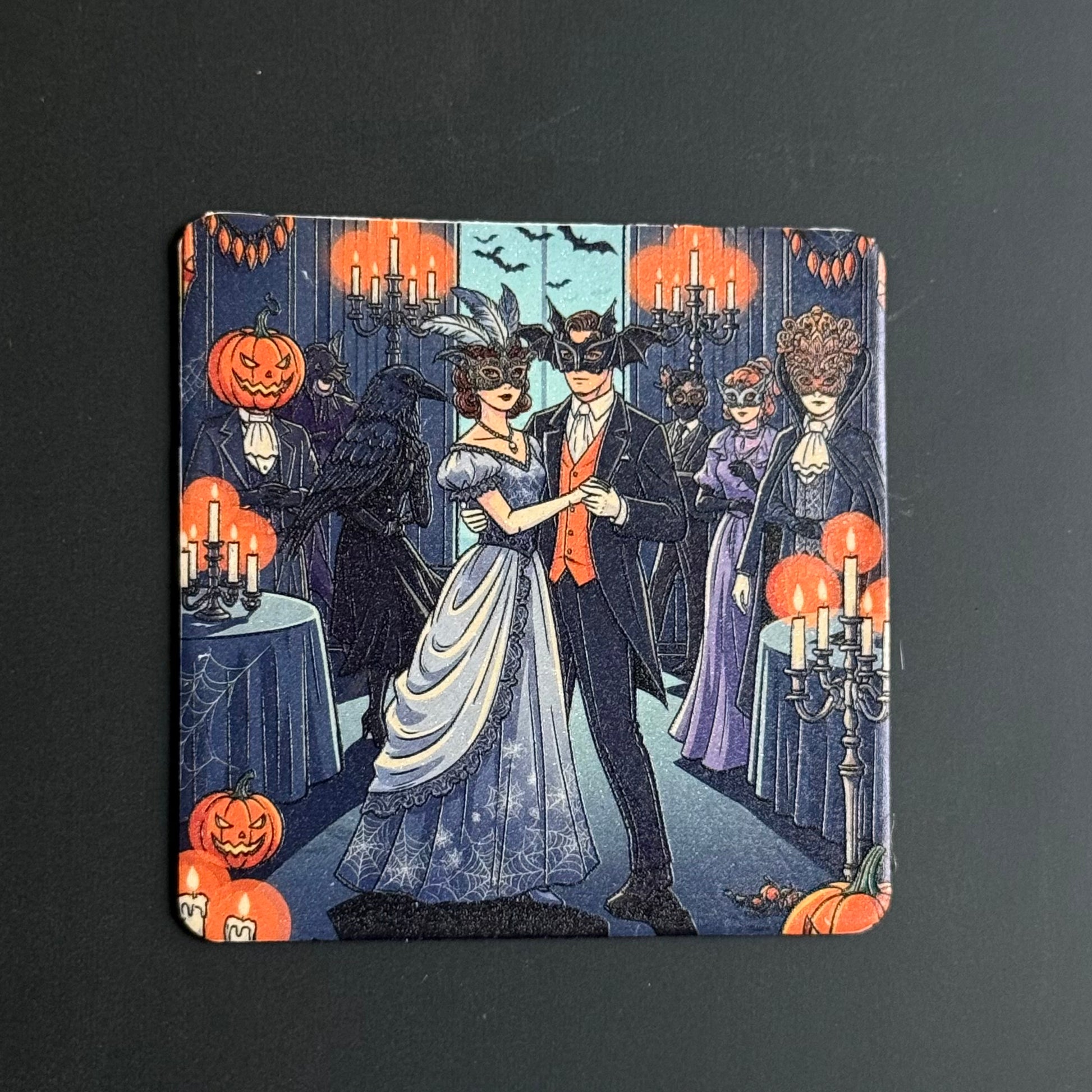 A square coaster featuring a vintage-style Halloween illustration with a dancing couple in the center, surrounded by jack-o'-lanterns, candelabras, and masked guests in a dimly lit hall.