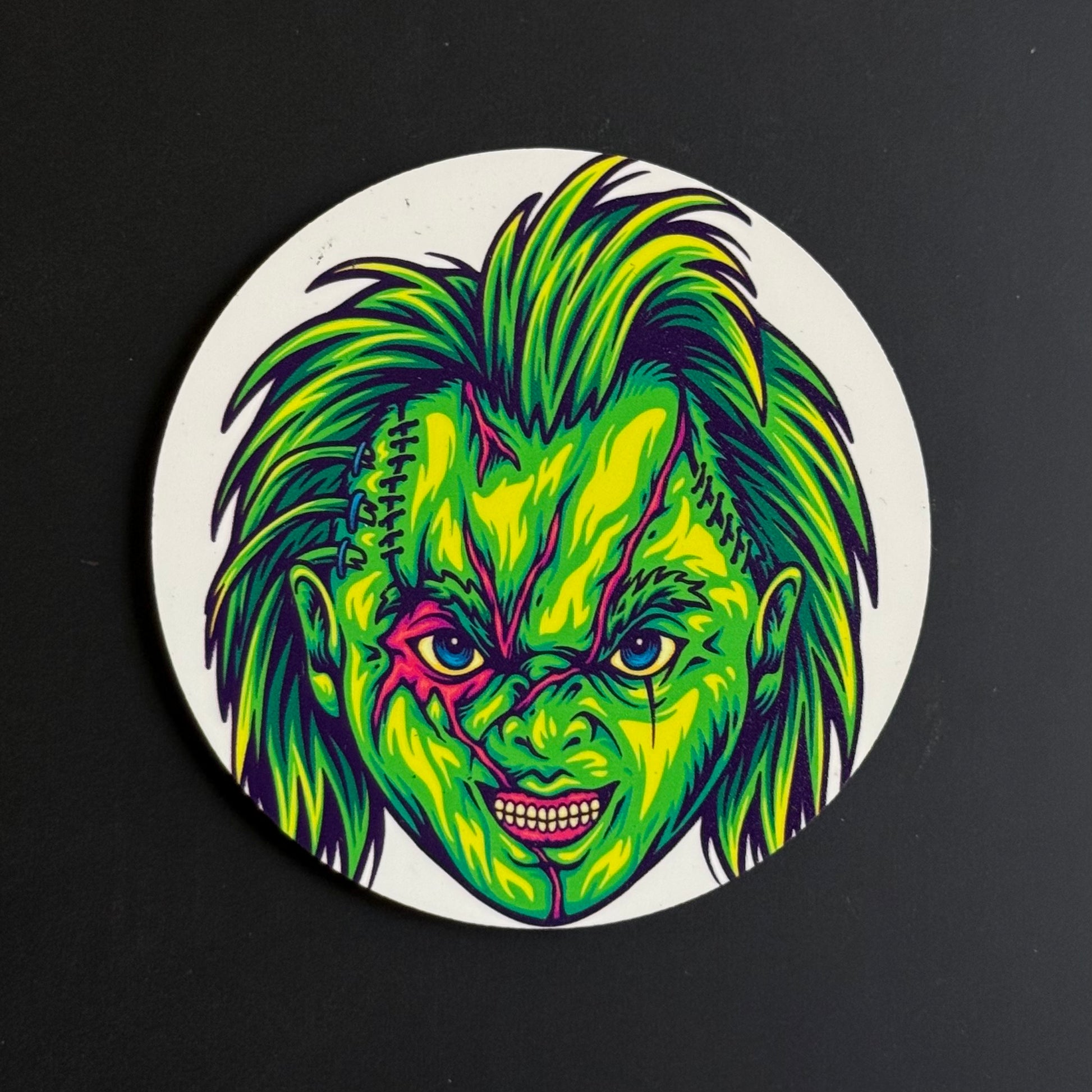A circular coaster featuring a vibrant, neon-style illustration of a horror character's face with green, yellow, and purple details, set against a dark background.