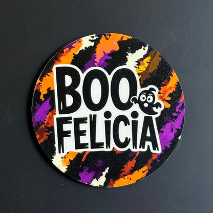 A circular sticker with a Halloween theme, featuring the text 'BOO FELICIA' in bold white letters with a small cartoon ghost. The background of the sticker has a colorful paint-splatter pattern in orange, purple, black, and cream.