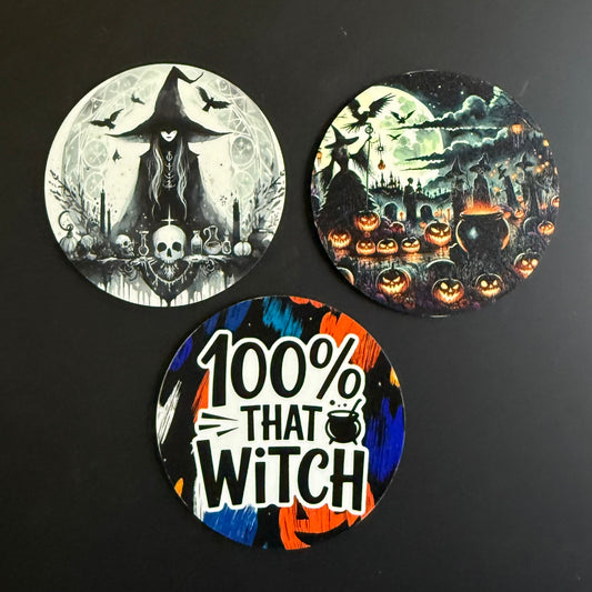 Three round Halloween-themed coasters displayed on a dark background. One coaster features a black and white witch and skull design under a full moon.
