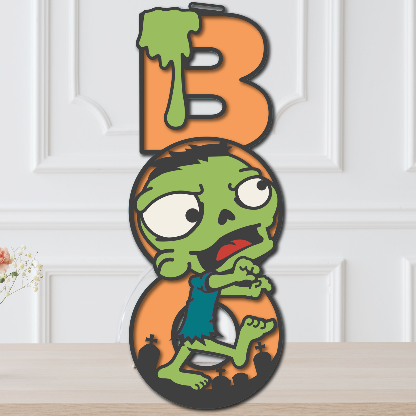Layered Zombie BOO Halloween door hanger with green zombie, orange lettering, slime, and graveyard details